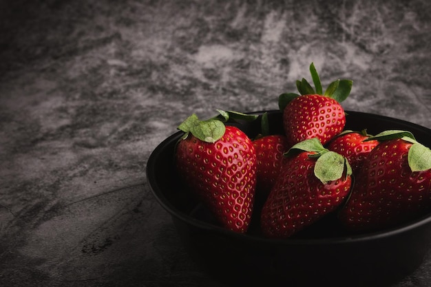 Fresas rojas frescas en un tazón. Frutas de fresa en el espacio de copia de mesa de piedra oscura para texto. vista superior.