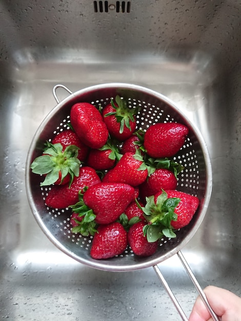 Fresas rojas jugosas maduras lavadas en un colador de malla encima del fregadero en la cocina, POV y vista superior