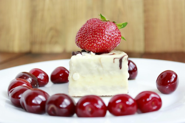 fresas rojas maduras y cerezas en el plato blanco y pastel en el fondo marrón fresas fresas y cereza en el plado