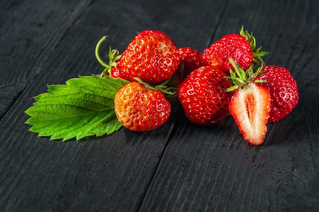 Fresas rojas maduras con hojas sobre un fondo negro Dieta dulce de verano y paquete de vitaminas saludables