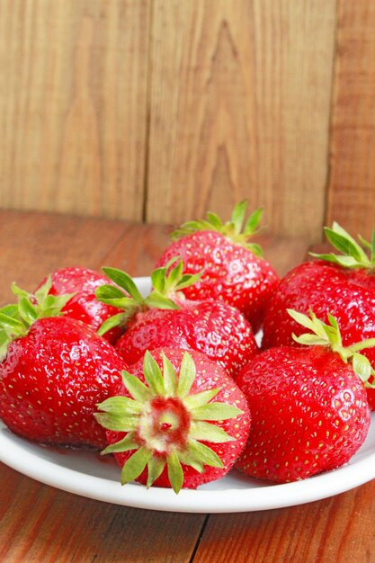 fresas rojas maduras en el plato blanco sobre el fondo marrón