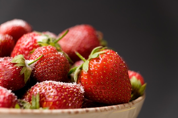 Fresas rojas maduras en un plato en un espacio de fondo negro para texto