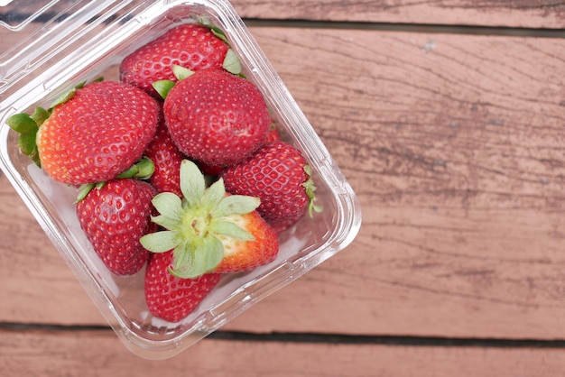 Fresas rojas maduras en un recipiente de plástico en la mesa