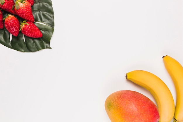 Fresas rojas en monstera y plátano con mango en esquina sobre fondo blanco