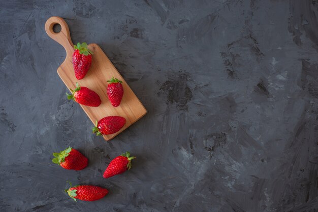 Fresas rojas en placa de madera sobre fondo negro, vista superior, flatlay con espacio de copia