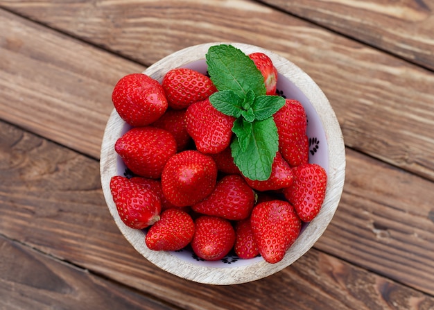 Fresas rojas en un recipiente sobre la mesa de madera en el jardín