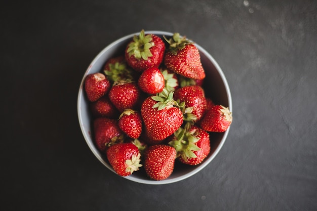 Fresas sabrosas maduras frescas en una placa negra sobre un fondo de madera gris. Endecha plana