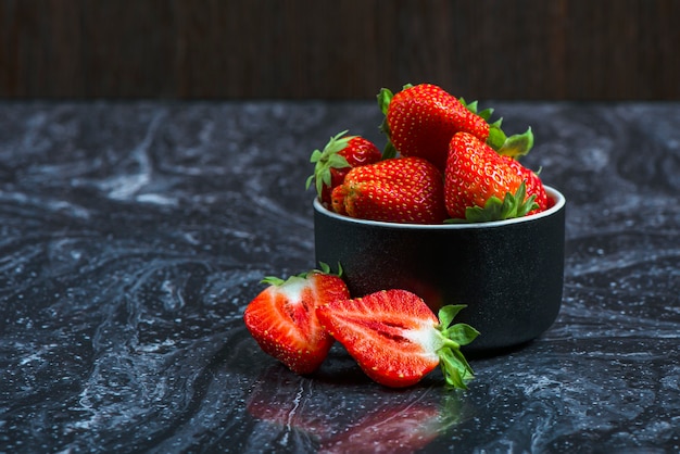 Fresas sobre mármol negro. Fresas maduras en un platillo sobre un fondo negro. Lugar para insertar texto.