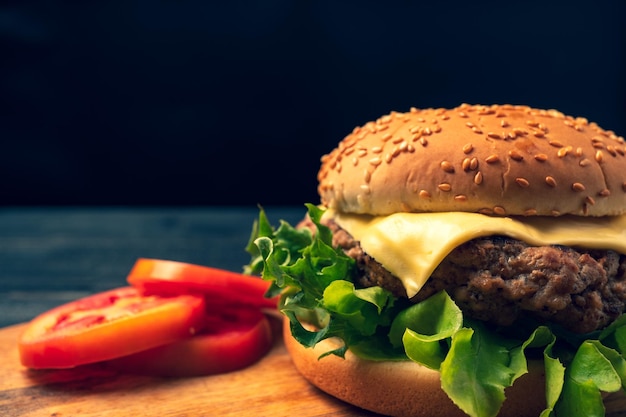 Foto fresca y sabrosa hamburguesa casera con queso fresco junto a tomates en rebanadas en una tabla de cortar