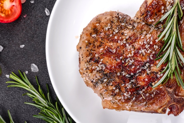 Fresco e delicioso bife suculento nos ossos com legumes e especiarias. grelha de bife suculento de porco na mesa escura