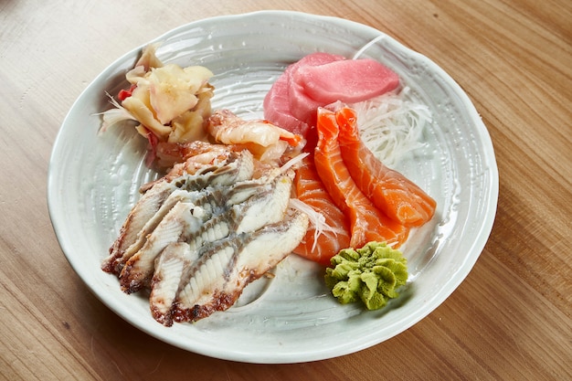 Fresco e delicioso camarão sashimi variado, atum, salmão e enguia com rabanete daikon e wasabi em uma tigela branca sobre uma superfície de madeira