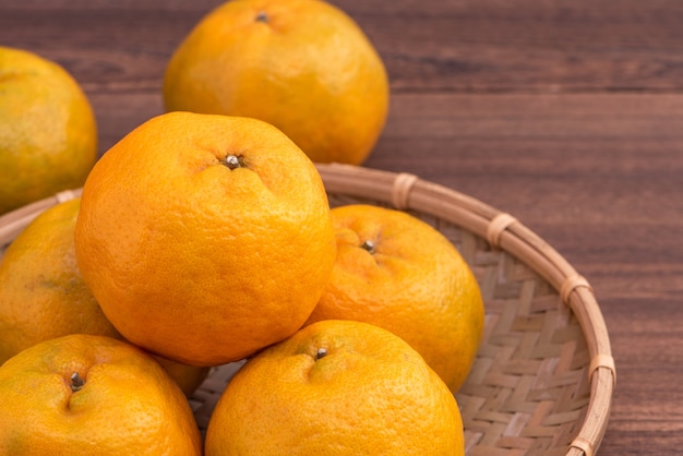 Fresco hermoso color naranja mandarina en un tamiz de bambú sobre la mesa de madera oscura.