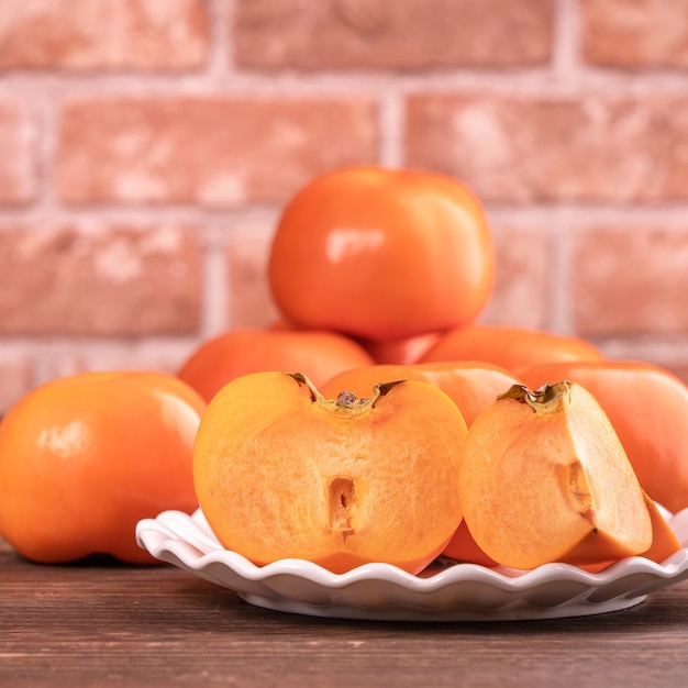 Fresco y hermoso kaki dulce caqui en rodajas en la mesa de madera oscura con fondo de pared de ladrillo rojo, concepto de diseño de fruta de año nuevo lunar chino, de cerca.