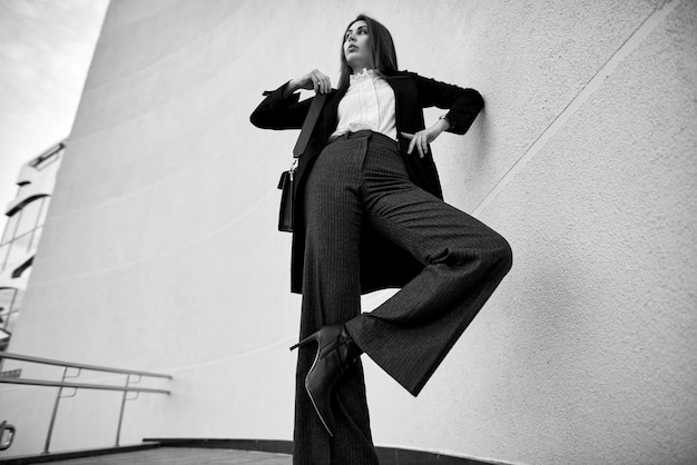 Fresco retrato de una mujer joven en una elegante chaqueta negra en una camisa cerca de un elegante edificio. Mujer en ropa casual de moda juvenil en la calle.