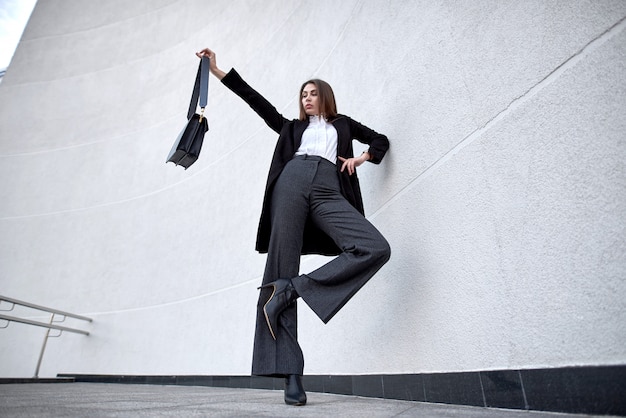 Fresco retrato de una mujer joven en una elegante chaqueta negra en una camisa cerca de un elegante edificio. Mujer en ropa casual de moda juvenil en la calle.