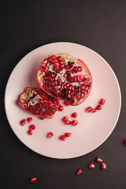 Foto fresco saboroso romã descascada doce com sementes vermelhas em chapa rosa sobre preto escuro