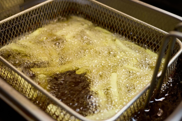 fresh potato strips are immersed in hot oil bubbling vigorously in a fryer the kitchen is busy as chefs prepare meals for the lunch service