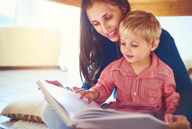 Freude an neuen Geschichten finden Aufnahme einer Mutter, die zu Hause mit ihrem kleinen Sohn ein Buch liest