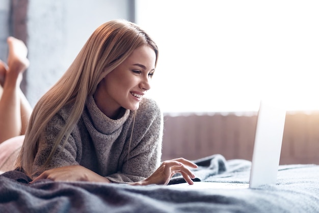 Freude und Ruhe. Schöne junge entzückte Frau, die sich entspannt und Laptop beim Lächeln benutzt.