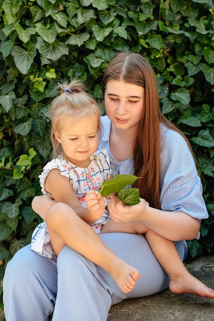 Freudige ältere Schwester, die jüngere Schwester hält, die Spaß hat und spielt und lacht Jugendlich Mädchen, das Babymädchen am Sommertag hält Kinder mit großem Altersunterschied Großer Altersunterschied zwischen Geschwistern