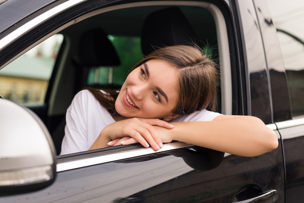 Freudige Frau, die ihren Ellbogen über Autofenster lehnt, während sie Straßenfahrt genießt