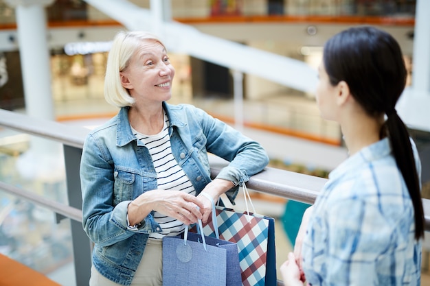 Freudige Frauen, die über das Einkaufen im Einkaufszentrum sprechen