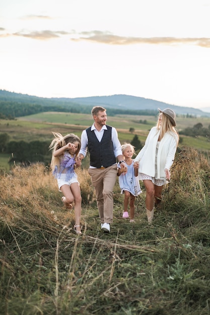 Freudige kaukasische Familie mit zwei Kindern, die Sommerwanderung im ländlichen Feld in den Bergen genießen