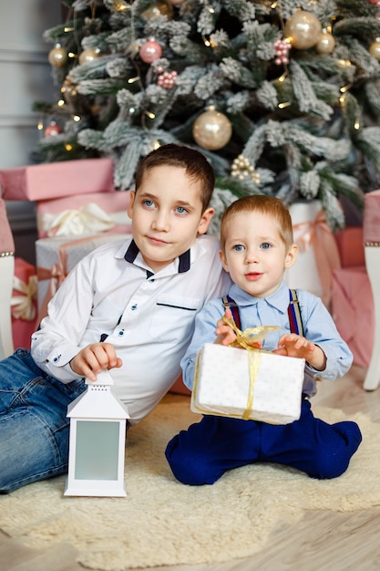 Freudige Kinder, die Weihnachtsgeschenke öffnen. Gemütlicher warmer Winterabend. Familie am Heiligabend. Kinder unter Weihnachtsbaum mit Geschenkboxen. Dekoriertes Wohnzimmer. Nette Kinder mit Weihnachtsgeschenkboxen zu Hause.