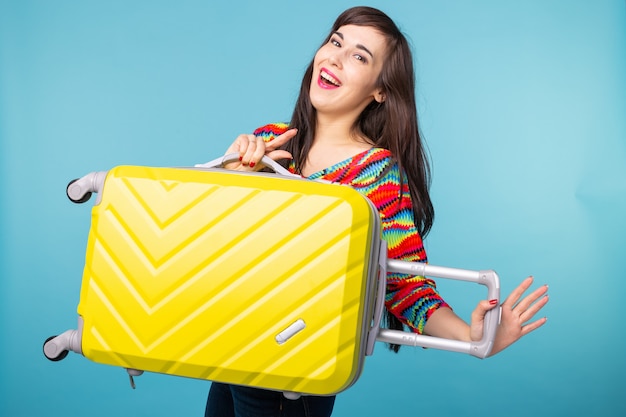 Freudige lächelnde junge brünette Frau, die mit einem gelben Koffer aufwirft