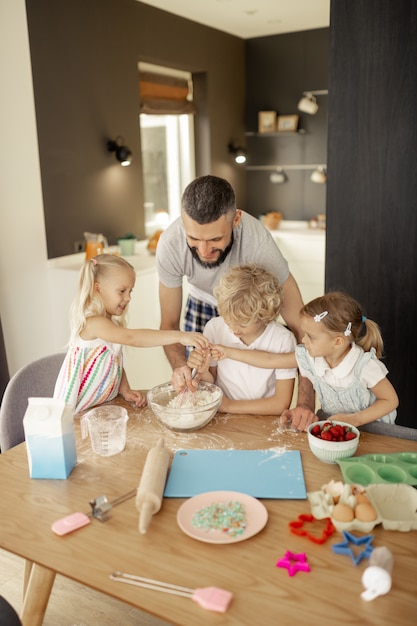 Freudige nette Kinder, die sich gegenseitig in der Küche helfen