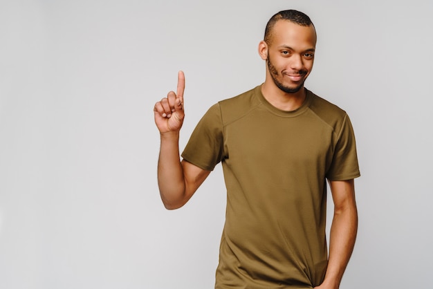 Freudiger freundlicher afroamerikanischer junger Mann im grünen T-Shirt, das EINEN mit den Fingern zeigt