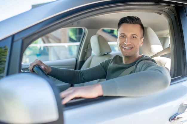 Freudiger junger Mann, der im Auto auf dem Fahrersitz sitzt