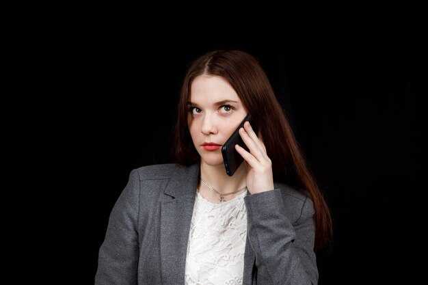 Freudiger und erfolgreicher junger Modeblogger telefoniert emotional. Schöne junge Frau in der lässigen grauen Jacke hält Smartphone.