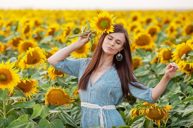 Freudiges Mädchen der Schönheit mit Sonnenblume, die Natur genießt und auf dem Feld der Sonnenblumen bei Sonnenuntergang lacht. Speicherplatz kopieren