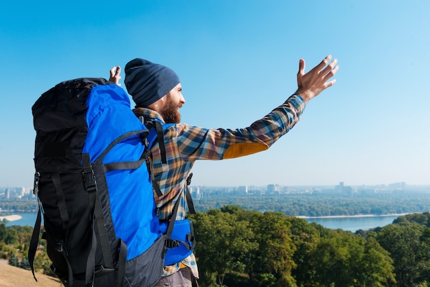 Freue mich ein Teil davon zu sein! Schöner junger Mann mit Rucksack und Blick mit erhobenen Armen