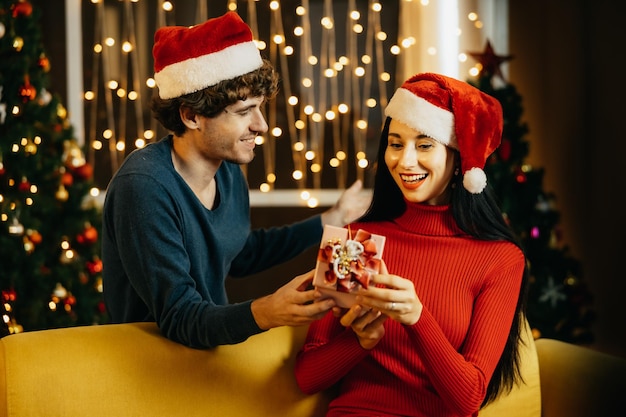 Freund, der seiner Freundin ein Weihnachtsgeschenk gibt. Junges Paar, das zu Hause feiert. Mann überrascht Frau.