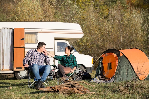 Freund küsst die Hand seiner Freundin auf dem Campingplatz mit Retro-Wohnmobil im Hintergrund.