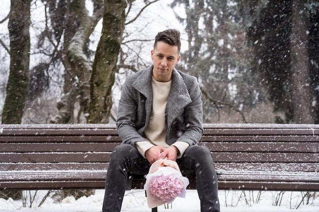 Freund mit einem Strauß rosafarbener Blumenhortensie wartet draußen auf seine Freundin, während Schnee fällt. Valentinstag-Konzept, Hochzeitsvorschlag. Mann geht auf ein Date.