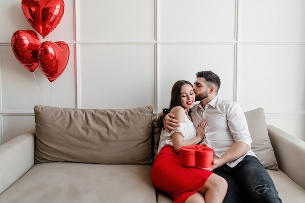 Freund und Freundin mit Herzen formten die Geschenkbox, die zu Hause auf Couch sitzt