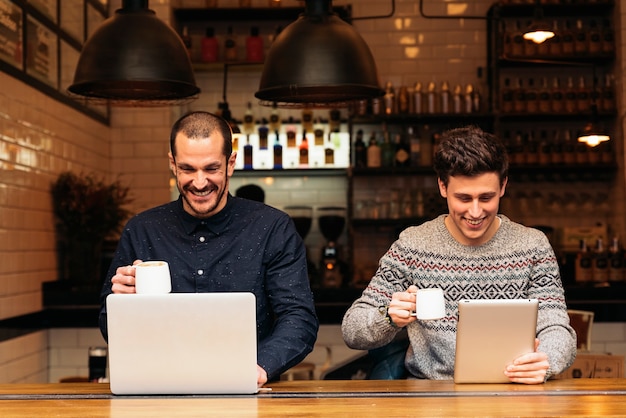 Freunde, die Handy und Laptop in einem Café benutzen.