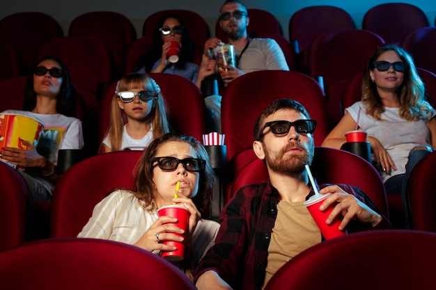 Freunde, die im Kino sitzen, sehen sich einen Film an, der Popcorn isst und Wasser trinkt.