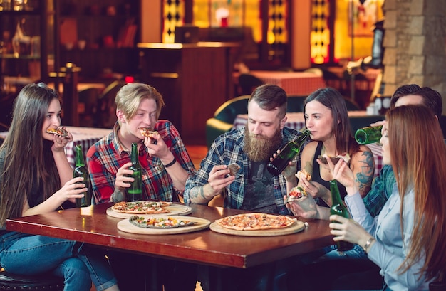 Freunde, die in einer Bar etwas trinken, sitzen an einem Holztisch mit Bier und Pizza.