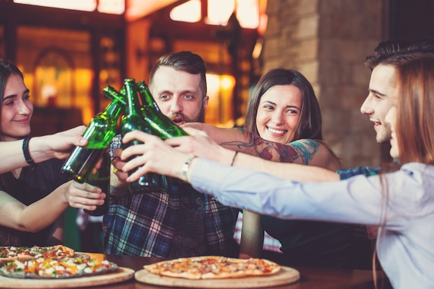 Freunde, die in einer Bar etwas trinken, sitzen an einem Holztisch mit Bieren und Pizza.