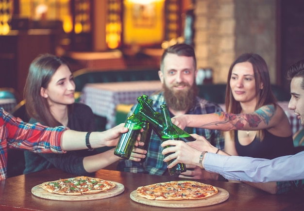 Freunde, die in einer Bar etwas trinken, sitzen an einem Holztisch mit Bieren und Pizza.