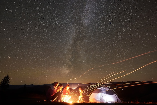 Freunde, die neben dem Lager ausruhen, Lagerfeuer unter dem nächtlichen Sternenhimmel