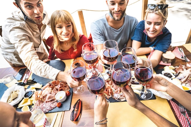 Freunde, die Rotwein in der Restaurantbar mit offenen Gesichtsmasken anstoßen