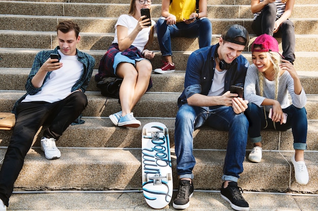 Freunde, die zusammen auf dem Treppenhaus unter Verwendung der Smartphones sitzen und kühlen