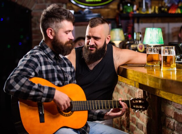 Freunde entspannen in Bar oder Kneipe Echte Männer Freizeit Hipster brutal bärtig verbringen Freizeit mit Freund in der Bar Mann spielt Gitarre in der Bar Fröhliche Freunde entspannen sich bei Gitarrenmusik Freitagsentspannung in der Bar