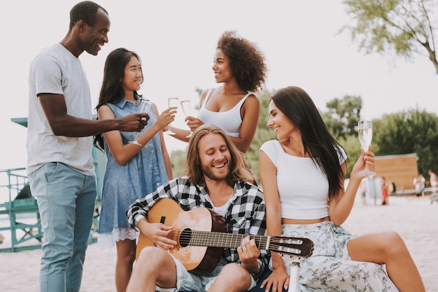 Freunde feiern am Strand Gitarre spielen.