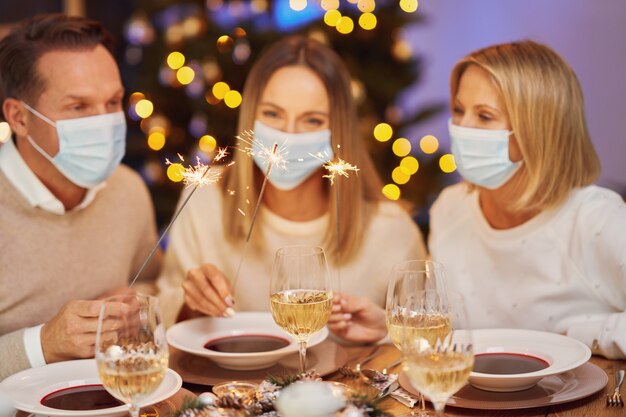 Freunde feiern Weihnachtsfeier mit Maske mit Wunderkerzen. Foto in hoher Qualität